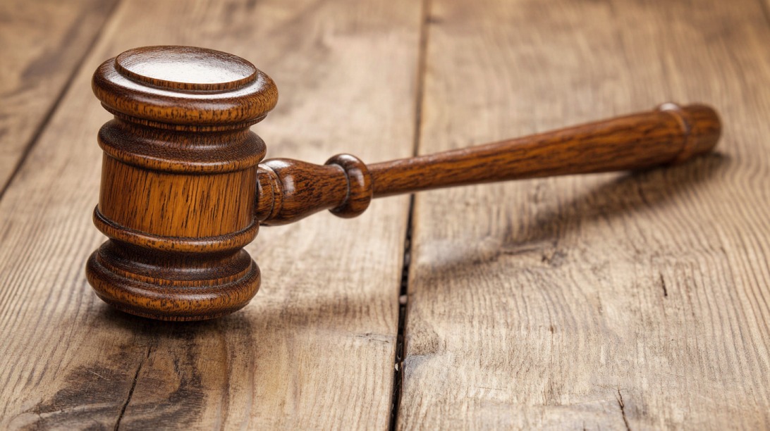 A wooden judge's gavel resting on a rustic wooden table