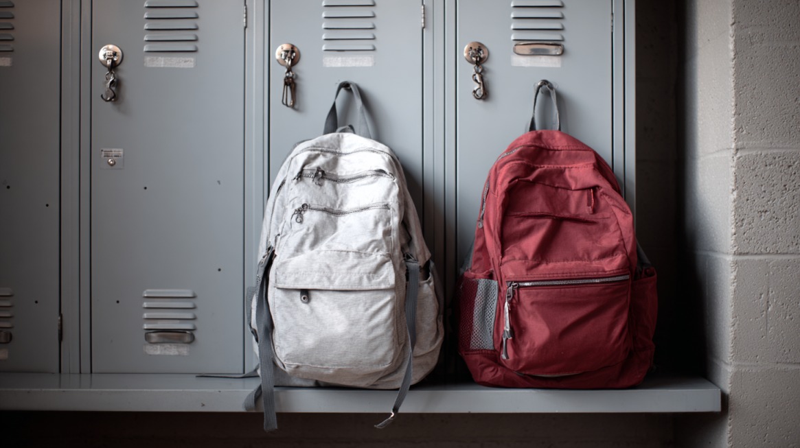 Two backpacks, one gray and one red, hanging in front of school lockers, symbolizing the difference between student privacy rights in backpacks and lockers