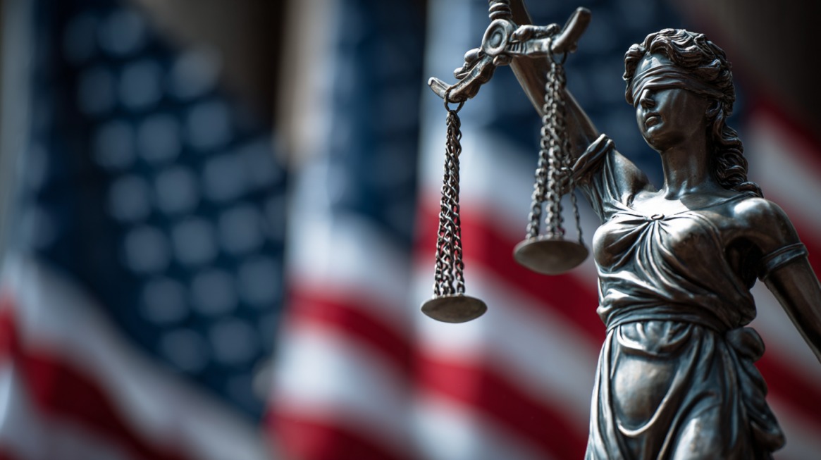 Statue of Lady Justice holding scales in front of blurred U.S. flags, symbolizing justice and legal rights in the United States