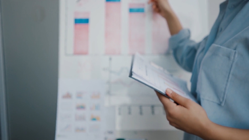 A person reviews financial charts and notes on a board, pointing to data while holding a report