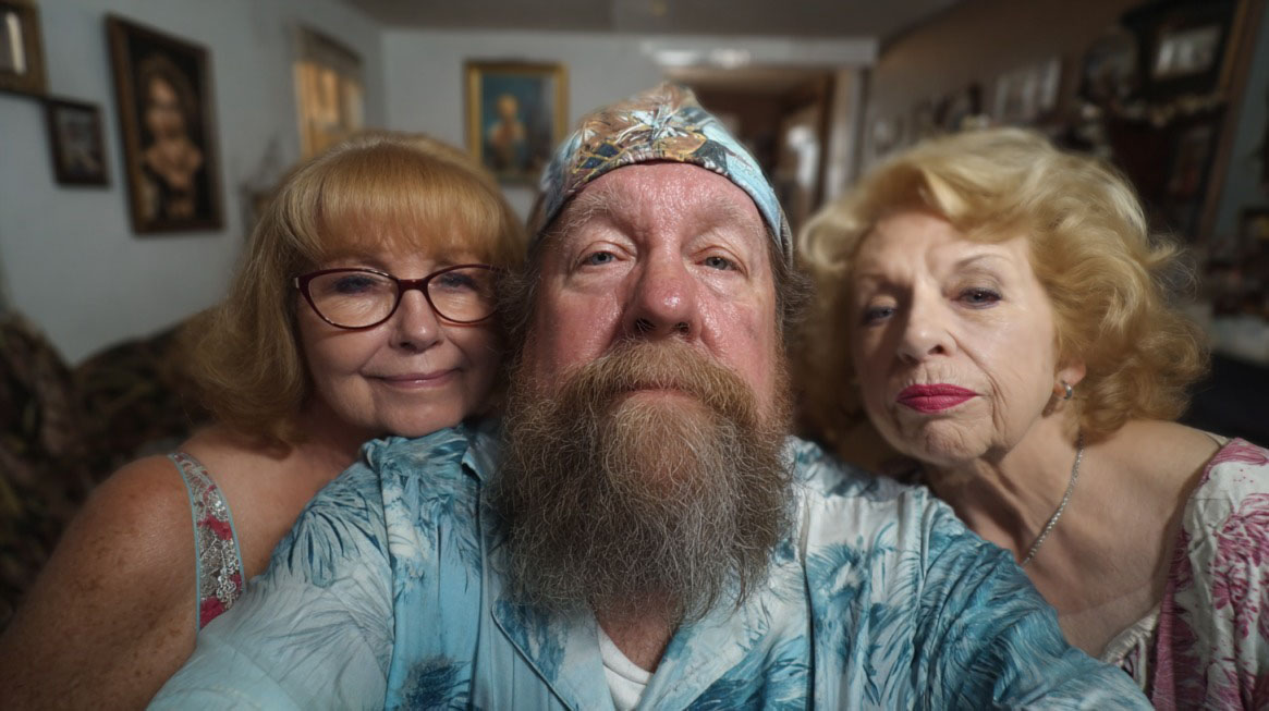 An older man with two women posing together, symbolizing polygamy and family arrangements