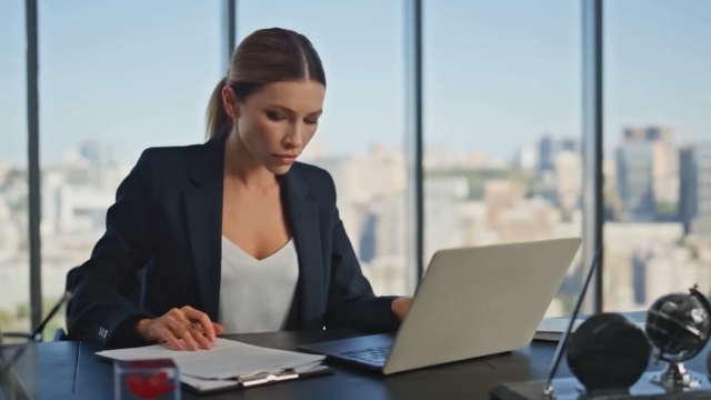 A businesswoman works on her laptop and paperwork during the H-1B visa employer registration process