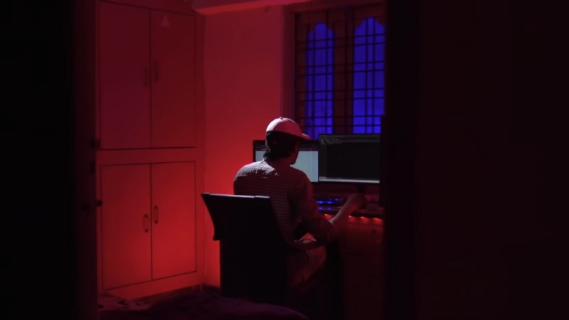 A person sits alone in a dimly lit room in front of multiple computer screens