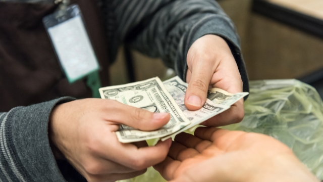 A person handing over cash in dollar bills during a payment transaction