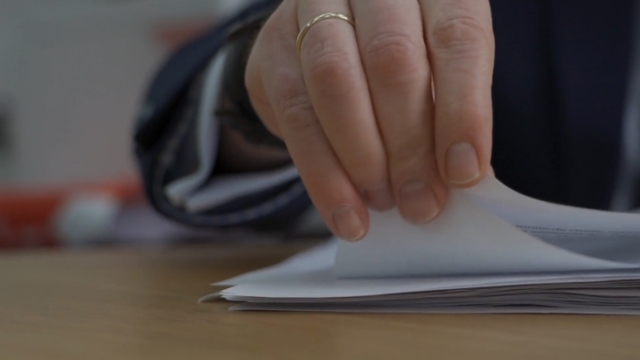 A close-up of a person reviewing and turning pages of official documents on a desk