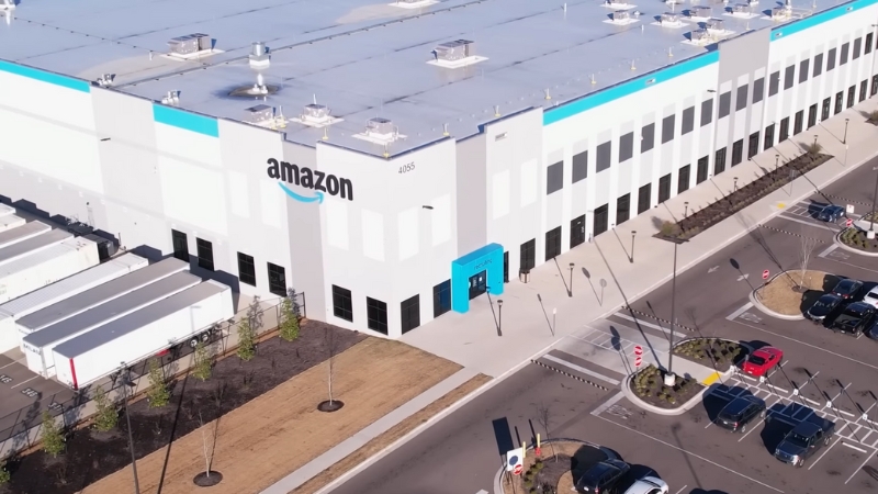 An Amazon warehouse with trucks and cars parked outside, representing the 2025 labor regulation case