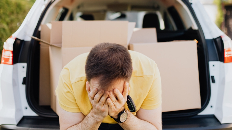 Man sitting in front of a car with boxes, showing the stress of moving without permission while on probation