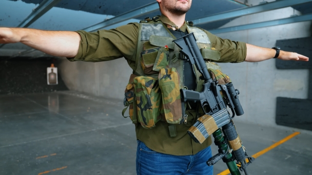A man at an indoor range wearing a tactical vest with a rifle equipped, showing legal protective gear
