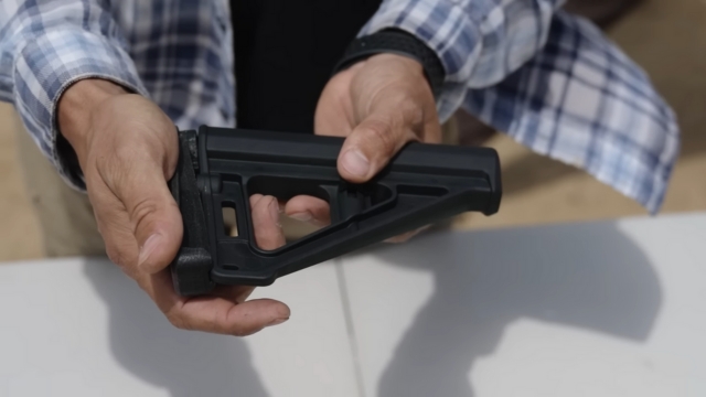 Hands holding a black firearm stock outdoors, showing a restricted gun accessory