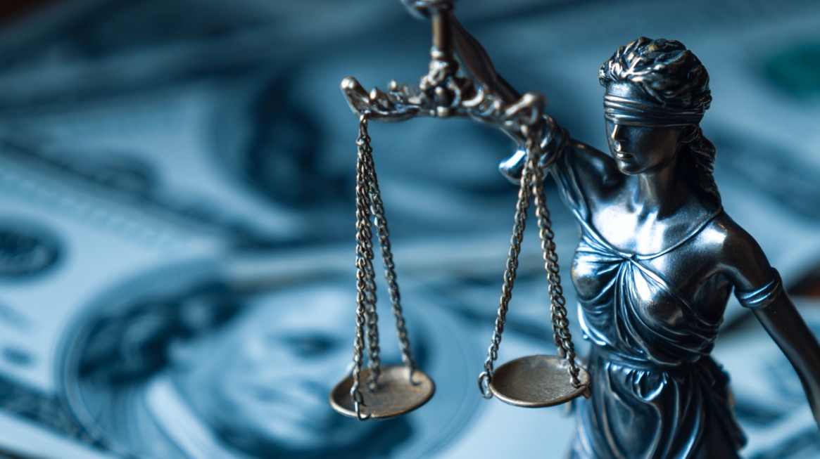 Statue of Lady Justice holding balanced scales in front of blurred money background