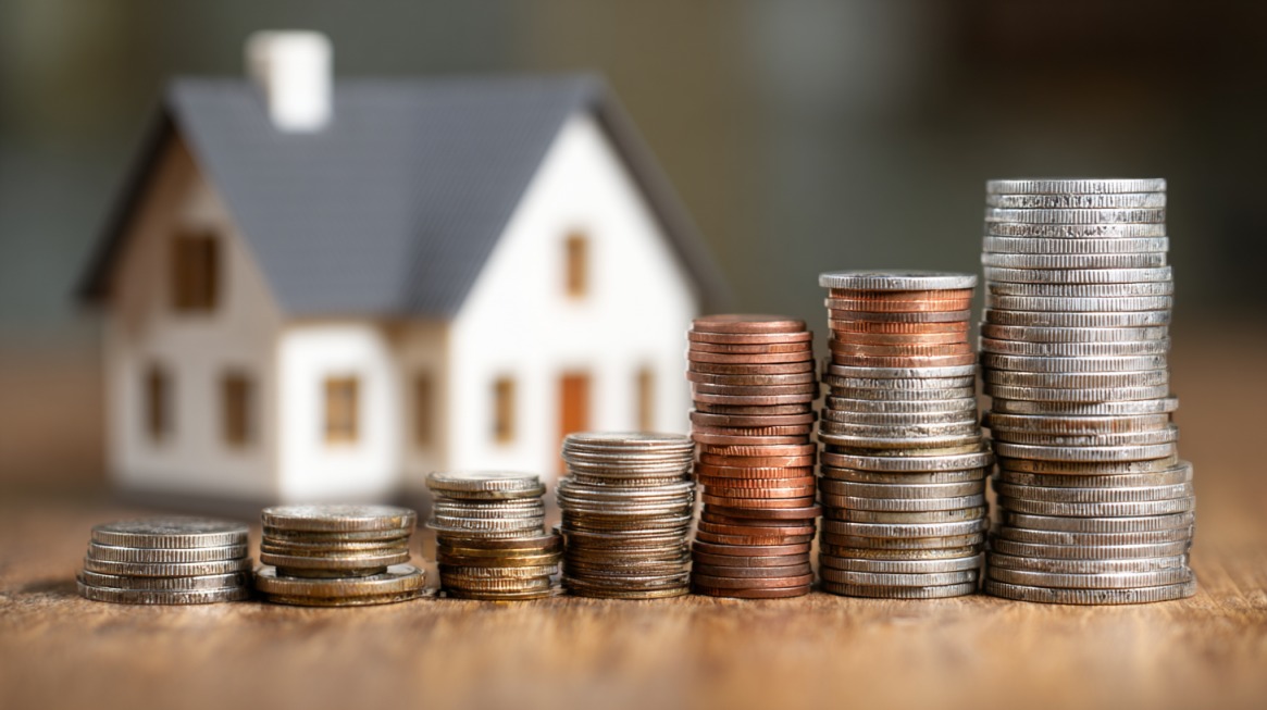 Stacks of coins arranged in increasing height with a small house in the background