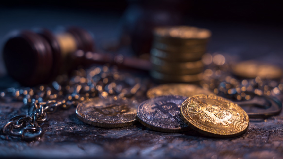 Cryptocurrency coins on a table beside a judge’s gavel and chain