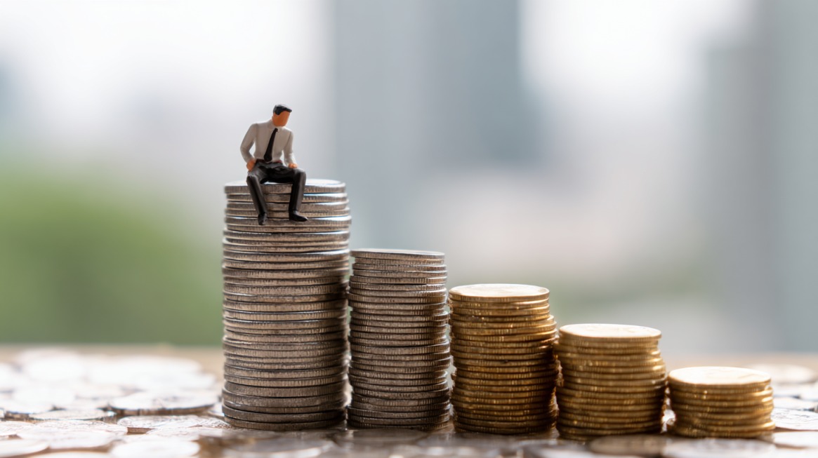 Small figurine of a businessman sitting on a tall stack of coins with shorter stacks beside it.