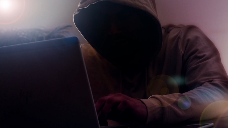 Hooded person using a laptop, showing how internet crime law relates to everyday online activity