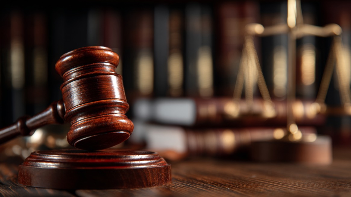 Judge’s wooden gavel on a desk with law books and scales of justice in background