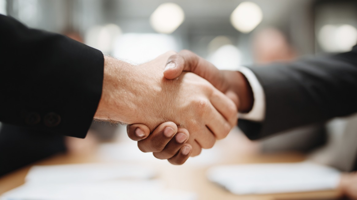 Two professionals shaking hands across a table in a business setting