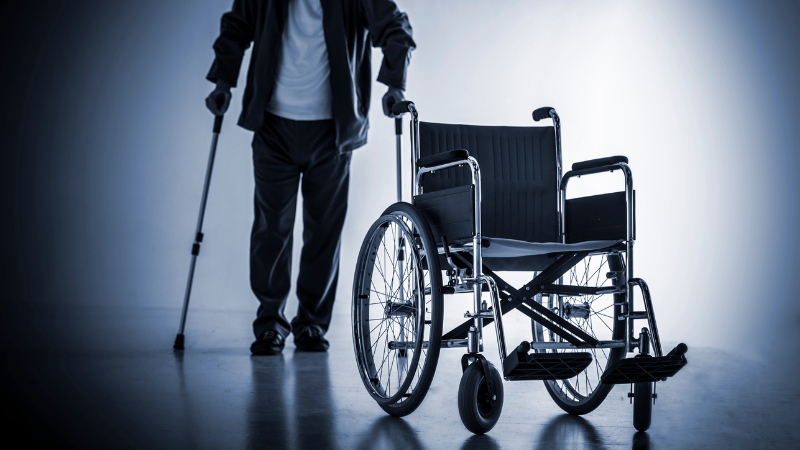 A person with a mobility disability stands beside a wheelchair