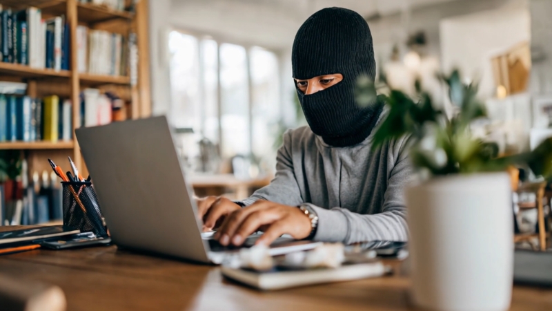 Masked person using a laptop at a desk, symbolizing wire fraud in internet crime cases