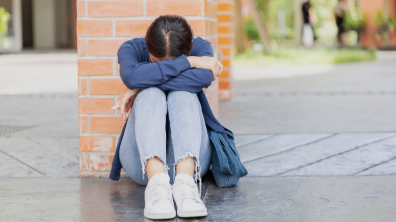 Student sitting alone outside a school building, showing emotional distress linked to a suspension dispute