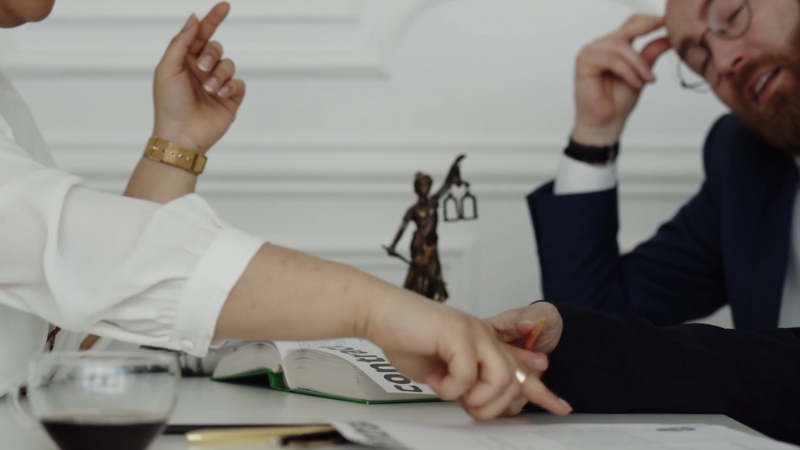 Two people in discussion over legal documents with a Lady Justice statue on the desk