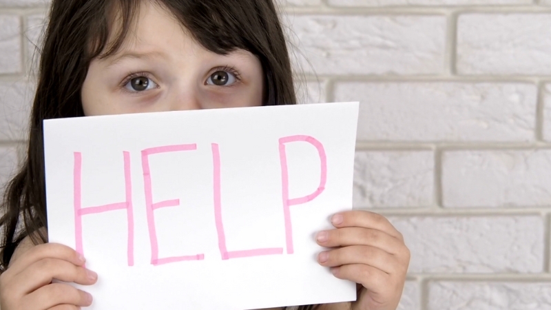 Child holding a sign that says “HELP,” highlighting the need for protection under the POCSO Act