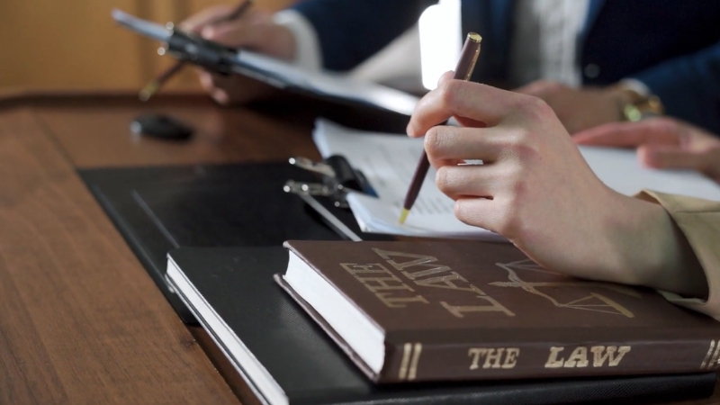 People reviewing legal documents beside a law book, representing school policies versus state law in mandatory reporting