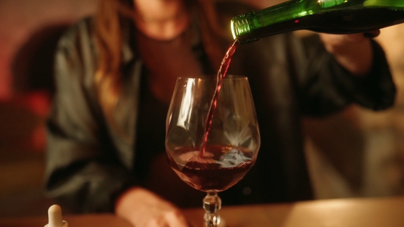 Person pouring red wine into a glass at a table, illustrating voluntary intoxication